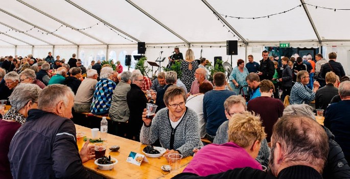 Mennesker sidder ved landbord i et stort telt og spiser